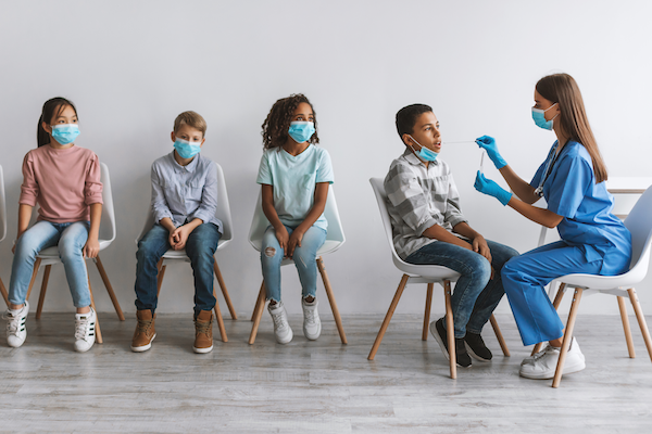 medical professional administering test to child while other children wait for testing